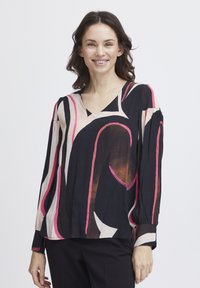 Blouse à manches longues et col en V, de couleur noire avec des motifs abstraits rose et crème. Fabriquée en tissu léger, elle offre une coupe décontractée et des manches à poignets.
