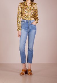 Blusa in satin a fantasia floreale gialla, jeans a vita alta di colore blu chiaro e mule in suede marrone con tacco a blocco. Outfit semplice e moderno.