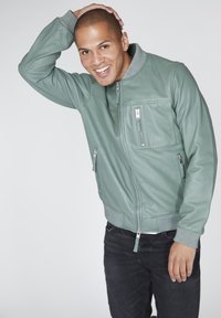 Světle zelená kožená bomber bunda s žebrovaným šedým límcem a manžetami, s kapsami na zip a elegantní, hladkou texturou.