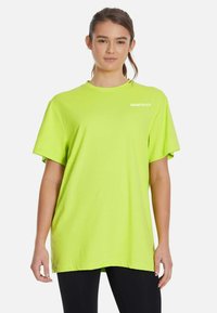 Neona zelena kratkotrajna majica s kratkimi rokavi, izdelana iz mehkega blaga, z okroglim izrezom in majhnim belim logotipom "SQUATPROOF" na zgornji levi strani.