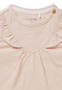 Zachte roze babyshirt met gerimpeld V-vormig biesdetail, een kleine gouden knop op de schouder en een ronde halslijn.