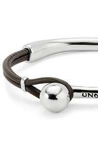 Pulsera tipo bangle con metal plateado pulido y una banda de cuero marrón oscuro que presenta una bola de plata y texto parcialmente grabado.