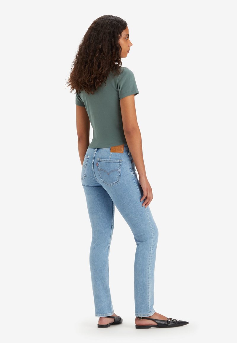 Camiseta verde ajustada combinada con jeans rectos de un azul claro, con una etiqueta de cuero en el bolsillo trasero y zapatos planos negros de punta.