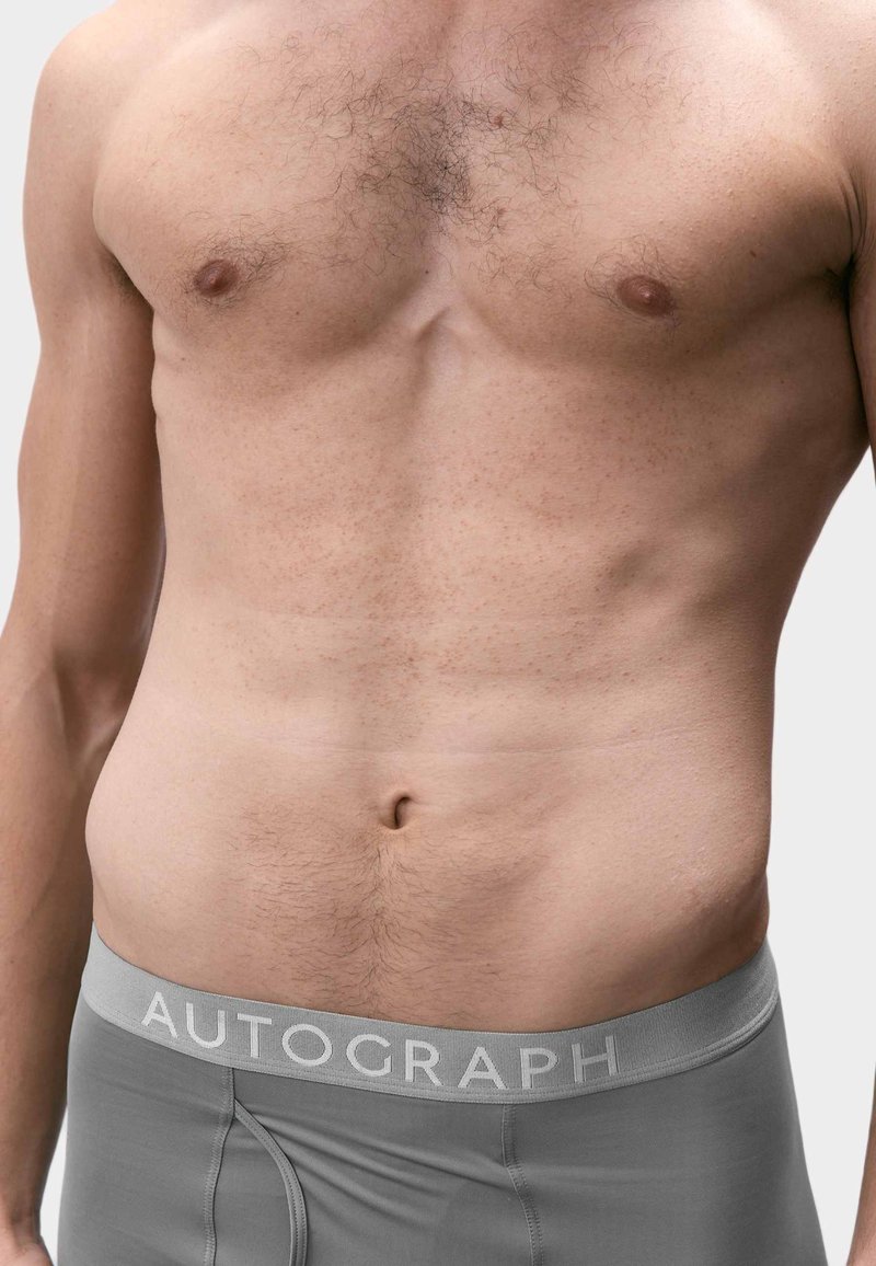 Primo piano del torso di un uomo che indossa boxer grigi AUTOGRAPH, mostrando peli sul petto e muscoli addominali visibili.