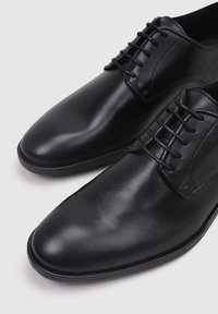 Zapatos de vestir de cuero negros con un diseño elegante, que presentan una textura suave, punta redondeada y cierre con cordones. Detalles de costura sutiles visibles.
