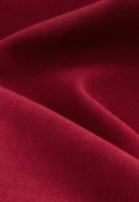 Piros szövet, közeli nézet. Puha textúra, sima felszín és enyhe nyúlás, egységes színnel és látható minták vagy díszítések nélkül.