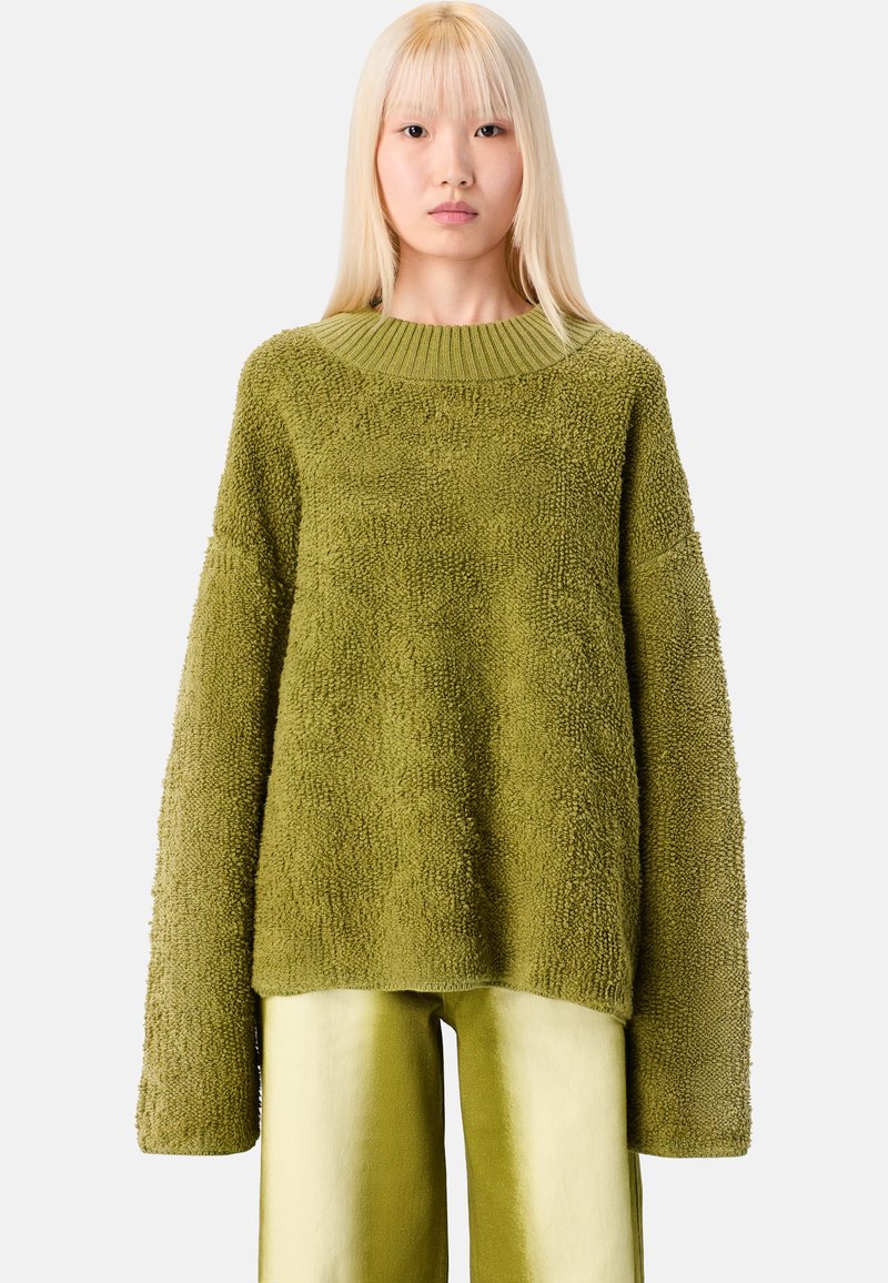 Vihreä tekstuuri neuletakki, jossa on leveä neulottu kaula-aukko ja pitkät hihat, yhdistettynä samanvärisiin vaaleanvihreisiin housuihin. Pehmeä kangas, ylisuuri istuvuus.