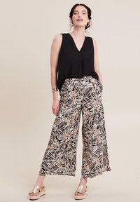 Zwart mouwloos topje met een V-hals, gecombineerd met wijde broek met een botanische print in zwart, wit en roségoud. Licht stoftextuur.