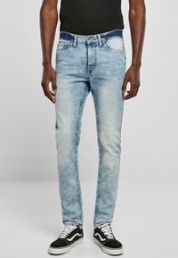 Jeans de mezclilla azul claro con un corte slim, diseño deslavado, cinco bolsillos y una cinturilla oscura, combinados con zapatillas en blanco y negro.