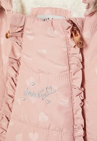 Roze pufferjas met hartjespatronen, gerimpelde randen en een zilveren geborduurde tekst "lovely." Heeft een gouden rits met een hartje detail.