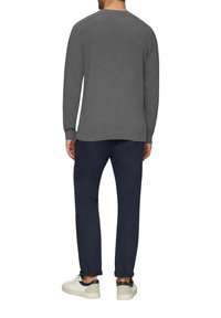 Un pull gris à manches longues avec des poignets côtelés, associé à un pantalon marine. Le modèle porte des baskets blanches avec des accents sombres.