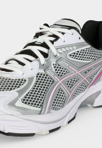 Chaussure de course en mesh blanc, argenté et rose avec lacets blancs et semelle coussinée, inclinée pour montrer le côté médial et l'avant.