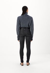 Szürke bordázott garbó pulóver hosszú ujjakkal, fekete skinny farmerrel párosítva. Az öltözék magas derekú és minimális varrási részletekkel rendelkezik.
