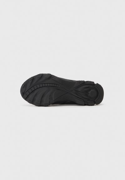 Suela de zapato deportivo negro con goma texturizada para agarre; presenta diseños curvados y surcos profundos para tracción en diversas superficies.