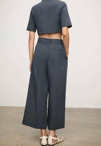 Top corto gris con mangas cortas combinado con pantalones anchos grises. El conjunto presenta un diseño limpio y un aspecto ajustado.