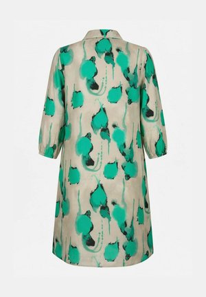 Beige mekko, jossa on kyynärtaipeeseen ulottuvat hihat ja vihreä-musta abstrakti kukkakuosi, kuvattuna takaa yksiväristä taustaa vasten.