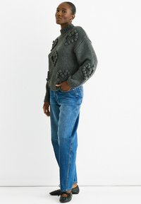 Gray knitted sweater with 3D bobble pattern, high neck, loose fit. Paired with blue straight-leg jeans and black flat shoes.