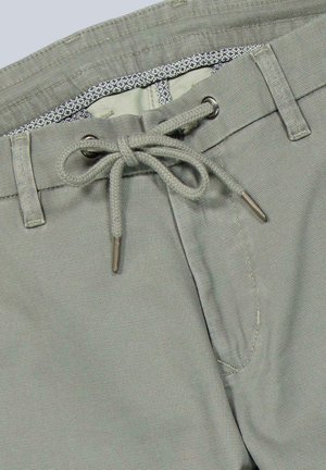 Hellgraue Hose mit Kordelzugbund, der zu einer Schleife gebunden ist und Metallspitzen hat. Die Hose verfügt über Gürtelschlaufen und einen sichtbaren inneren gemusterten Taillenbund.