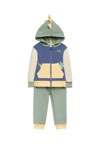 Conjunto de dos piezas con capucha que incluye una chaqueta azul y crema con púas de dinosaurio y un bolsillo amarillo, combinada con pantalones verdes.