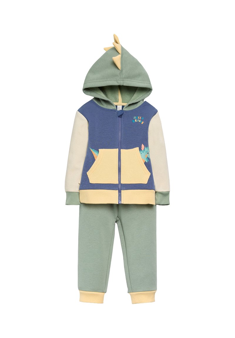 Conjunto de dos piezas con capucha que incluye una chaqueta azul y crema con púas de dinosaurio y un bolsillo amarillo, combinada con pantalones verdes.