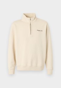 Μπεζ φούτερ με φερμουάρ μέχρι το ένα τέταρτο, υψηλό γιακά και μικρό μαύρο λογότυπο κειμένου στο αριστερό μέρος του στήθους που γράφει "Abercrombie & Fitch".