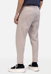 Jasnobeżowe spodnie o zwężanym kroju, wykonane z teksturowanej tkaniny. Posiadają tylne kieszenie i podwinięte nogawki, zestawione z czarnymi trampkami.