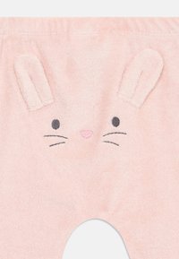 Pink child's pants made of soft, textured fabric featuring a bunny face design with embroidered eyes, nose, and ears on the waistband.