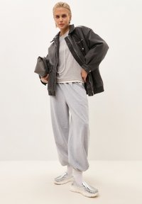 Přes oversized černou koženou bundu, šedé tričko, šedé tepláky a metalické slip-on boty; vrstvené textury a neutrální barvy.