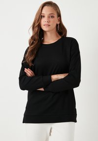 Fekete, hosszú ujjú pulóver kerek nyakkivágással, puha tapintással és bordás mandzsettákkal, laza szabással és enyhén hosszabbított aljjal.
