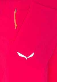 Tela roja con una textura suave presenta un cordón naranja y un diseño de logo blanco, colocado en la parte superior de un artículo.