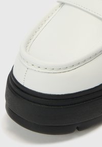 Mocasini albi din piele cu talpă de cauciuc neagră. Prezintă o cusătură și o textură netedă. Design cu vârf rotunjit și accente minimale.