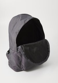 Sac à dos gris avec un extérieur en tissu texturé, un haut ouvert et un intérieur noir. Le design comprend une capuche douce et arrondie et une fermeture éclair.