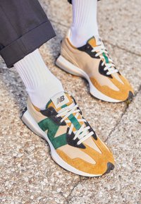 New Balance lenkkarit beige, ruskeassa ja vihreässä, joissa on teksturoitu mokka ja nailonpinta, valkoiset nauhat ja pehmustettu pohja.