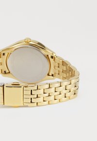 Goldene Metall-Uhr mit einem Armbanddesign aus Gliedern. Glatte, polierte Oberfläche mit einem runden Gehäuse und einem schlichten, reflektierenden Rückseitenteil.