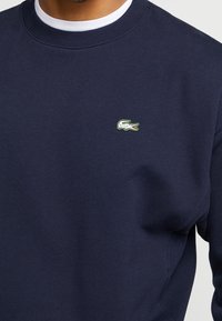 Sudadera azul marino hecha de tela suave, con cuello redondo, puños acanalados y un pequeño logo verde de cocodrilo de Lacoste.