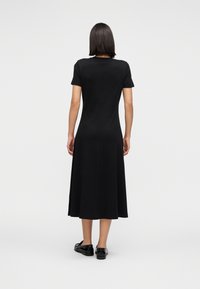 Μαύρο φόρεμα με κοντά μανίκια και ίσια γραμμή, που φτάνει κάτω από το γόνατο. Ομαλή, απαλή υφή, ελάχιστες ραφές, και απλός σχεδιασμός. Απλή πλάτη.