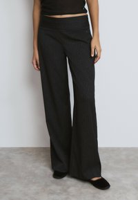 Pantalones negros de pierna ancha con rayas en colores claros, cintura alta lisa y un corte relajado. Textura suave, adecuada para un uso casual.
