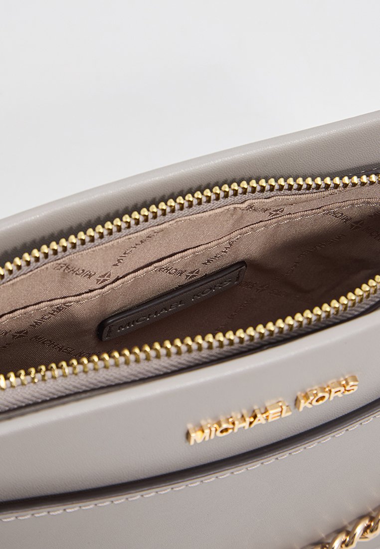 Beige Michael Kors handtas met gouden rits, gedeeltelijk geopend, waarbij de beige stoffen voering met een merkpatroon en het interne logo-label zichtbaar is.