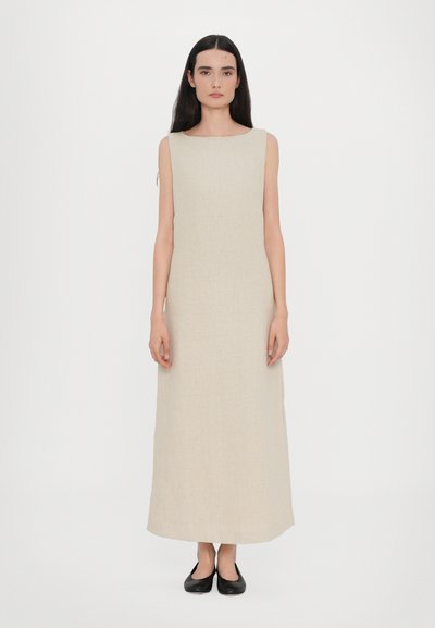 Vestido maxi sin mangas de color beige con escote cuadrado, hecho de una tela texturizada. Combinado con zapatos planos negros. Diseño minimalista, silueta recta.