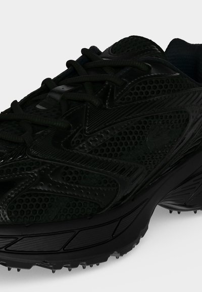Baskets de sport noires avec dessus en mesh et synthétique, fermeture à lacets à l'avant, et semelle texturée avec petits crampons pour l'adhérence.