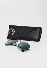 Ray-Ban sunglasses with dark tinted lenses, gold metal accents, and black plastic frames. Comes with a textured black protective case.