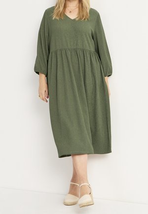 Zielona sukienka do kolan z dekoltem w serek, rękawami do trzech czwartej, marszczonym pasem i teksturowanym materiałem. Połączona z beżowymi espadrylami.