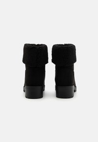 Bottes noires avec un col en polaire doux et texturé, en suédine. Talon bloc et semelle extérieure noire lisse, conçues pour le confort et la chaleur.
