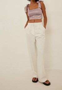 Top corto viola chiaro con spalline larghe, abbinato a pantaloni bianchi a vita alta e infradito nere. Tessuto morbido, vestibilità rilassata.