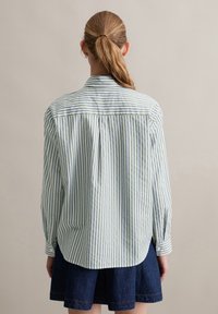Camicia a righe verde e bianca con colletto, maniche lunghe, polsini abbottonati e orlo curvo, realizzata in tessuto leggero.