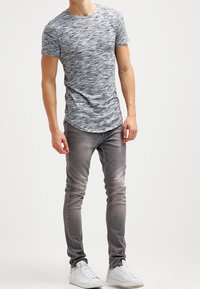 Šedá a bílá melírovaná trička s krátkým rukávem, v kombinaci s úzkými, světle šedými džíny a bílými teniskami. Hladká textura a neformální design.