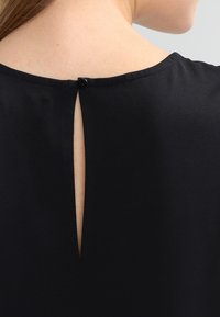 Zwarte top met een keyhole-opening aan de achterkant die met een knop is vastgezet. Zacht van structuur en een gladde stof met een schoon, eenvoudig ontwerp.