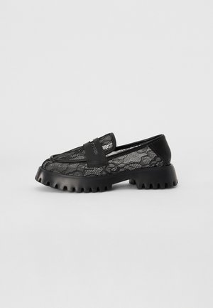 Svarta spetsiga loafers med en kraftig svart gummisula, med ett slätt läderband över ovansidan för extra detalj.