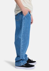 Light blue baggy jeans with a classic five-pocket design, denim texture, and rolled cuffs, paired with black sneakers featuring white soles.