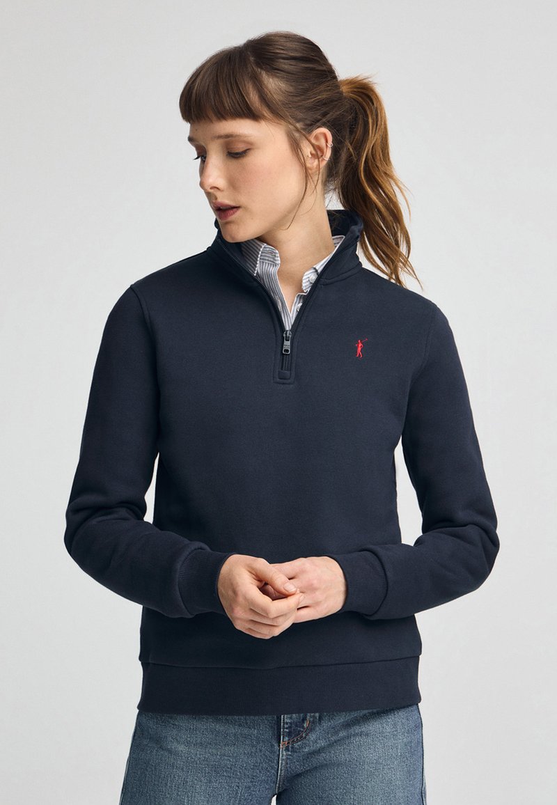 Felpa con zip colore navy realizzata in tessuto morbido, caratterizzata da un collo alto, polsini a costine e un piccolo logo rosso sul petto.